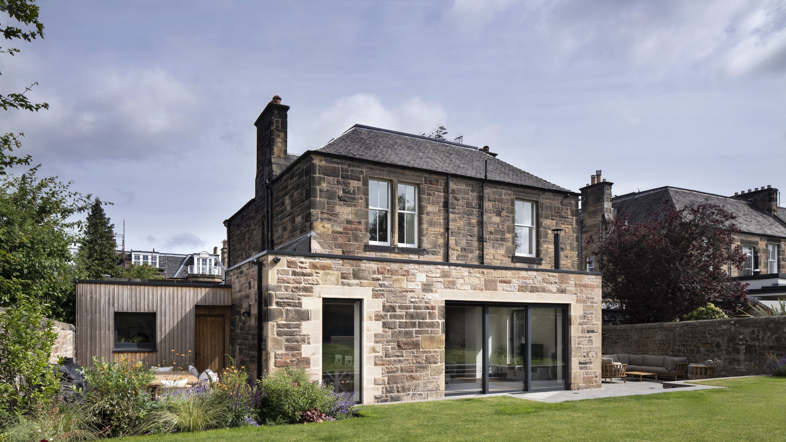 Sandstone extension with large glazing doors and terrace leading to garden