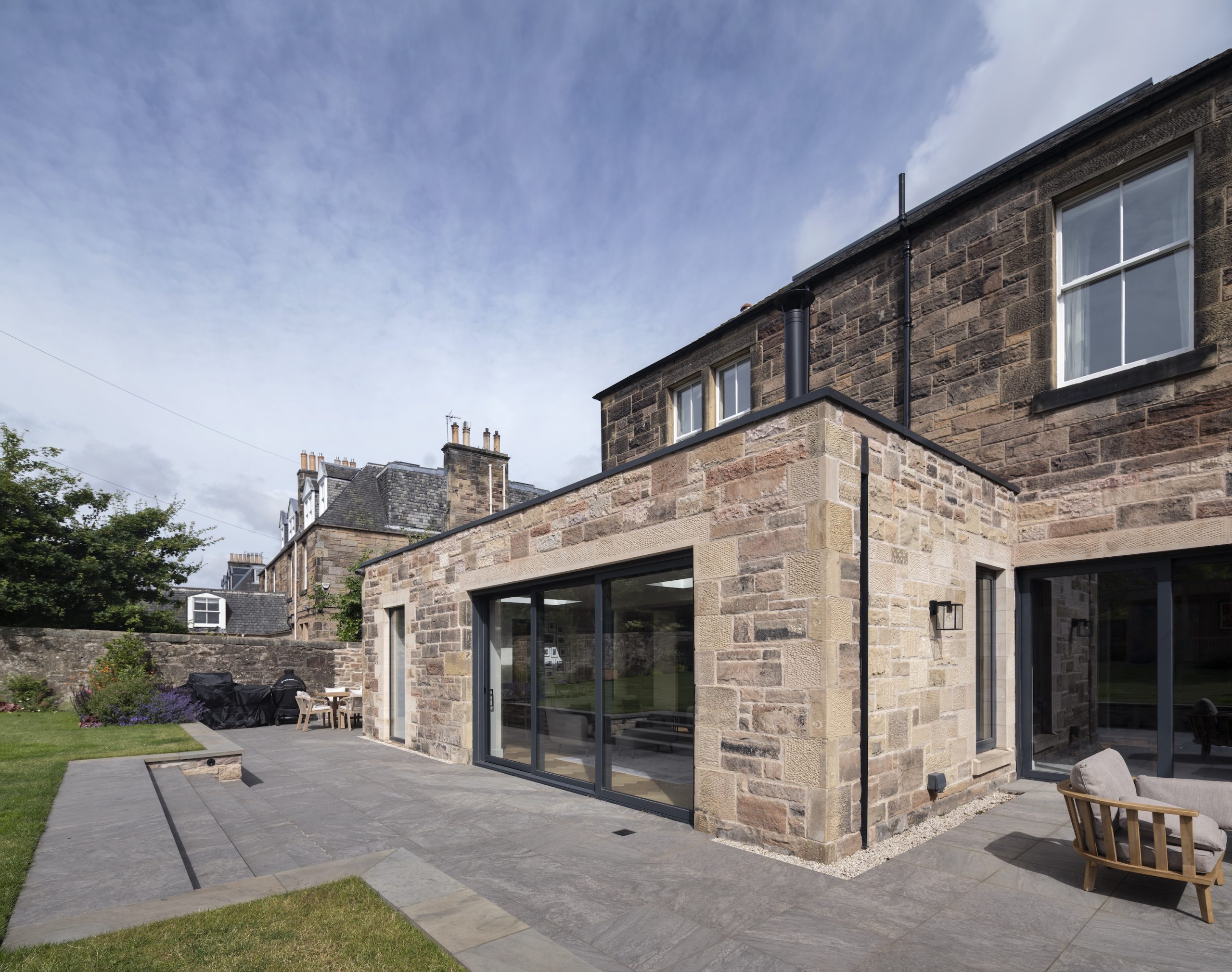 Sandstone extension with large glazing doors and terrace leading to garden