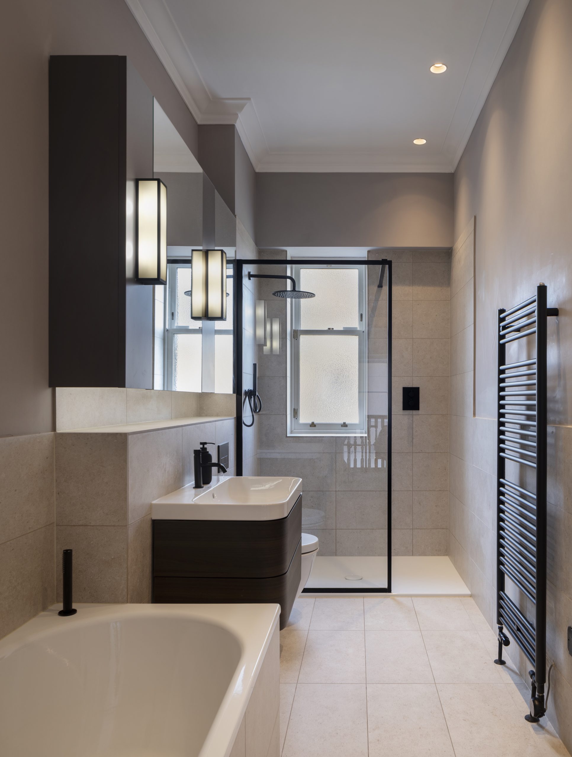 Family bathroom with limestone effect tiles, black brassware and bespoke mirror cabinet